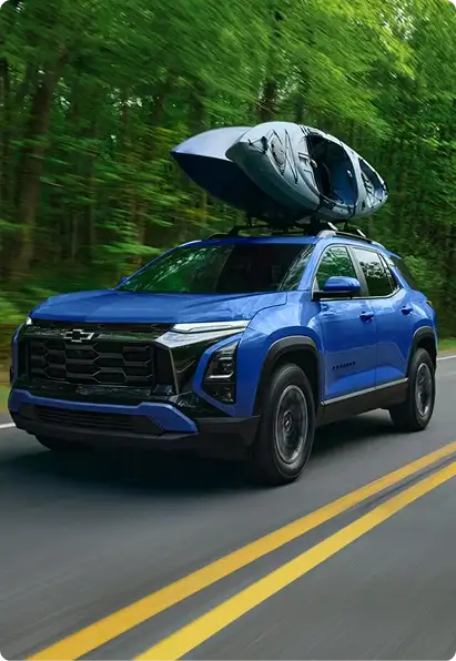 Blue Chevrolet Equinox carrying a kayak on its roof rack on a forest road