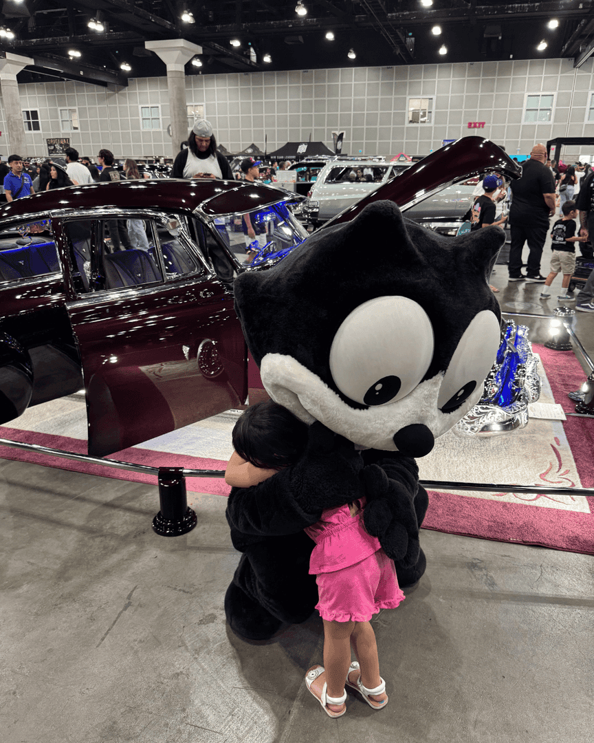 A young car show attendee hugging Felix the Cat at a Los Angeles community event