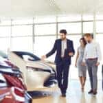 Happy couple and the dealer selling cars look the car in the showroom. Buying rental a car.