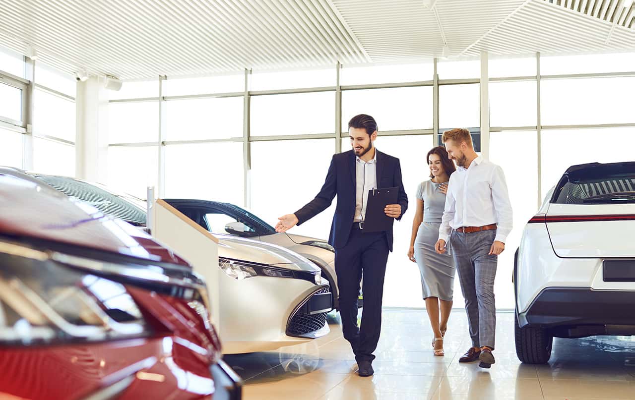 Happy couple and the dealer selling cars look the car in the showroom. Buying rental a car.