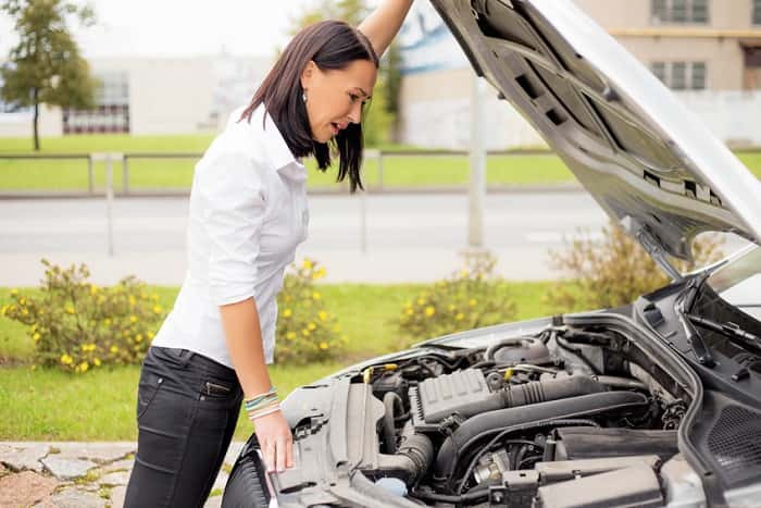 Woman looking under the hood of her broken car