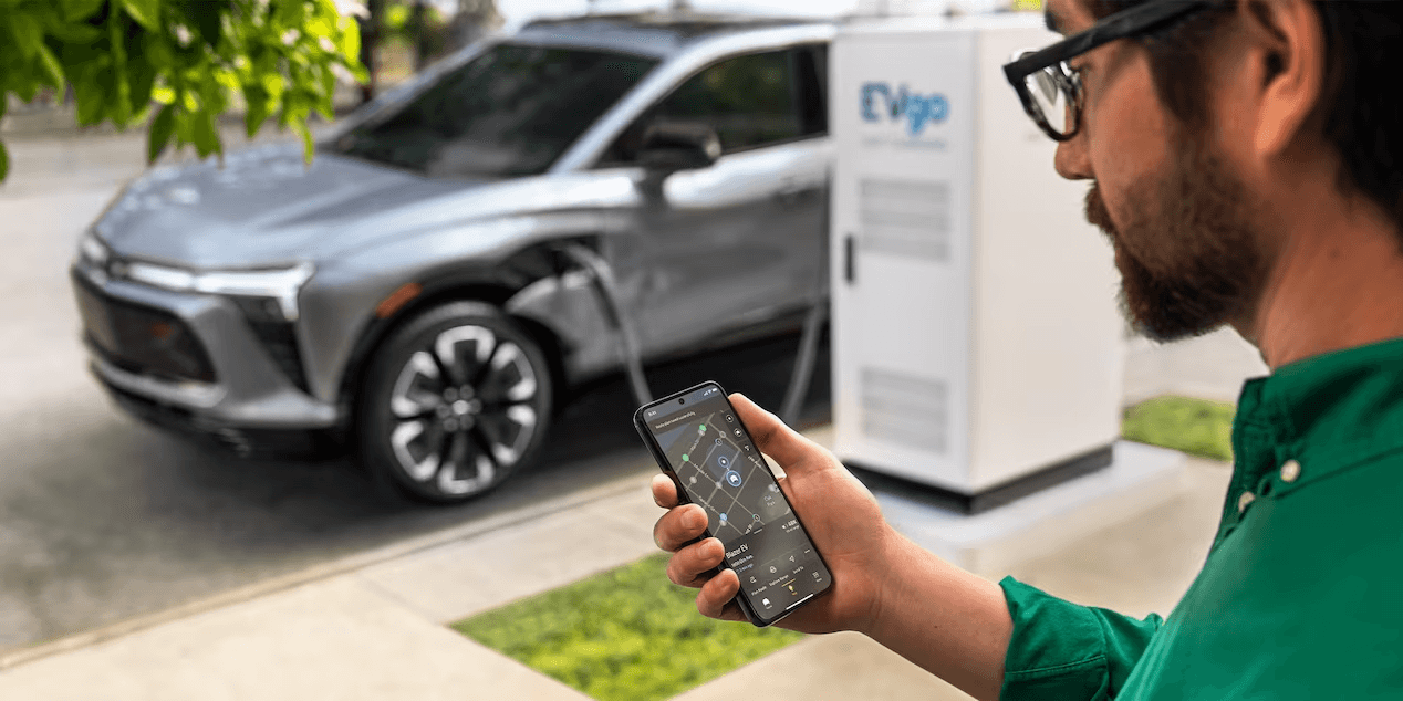 Man holding phone with a map displayed on screen with a charging electric-SUV in the background
