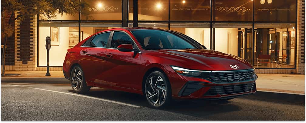 Red 2026 Hyundai Elantra sedan parked on a city street, shown from a front three-quarter view.