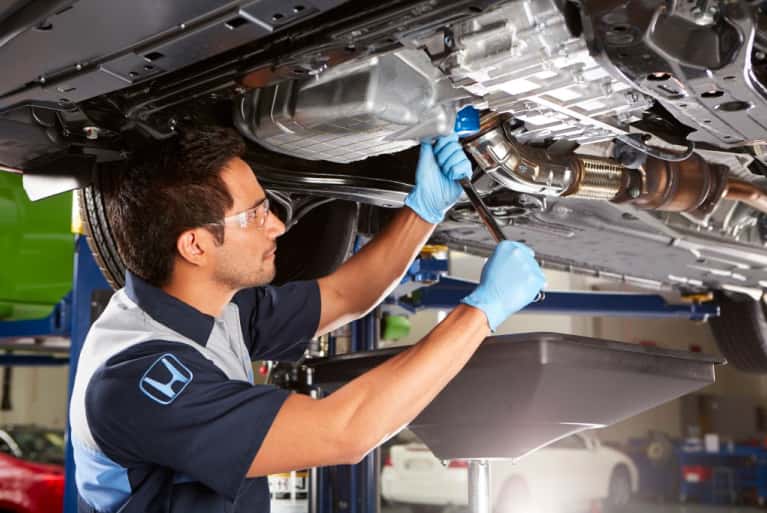 Honda service technician working on the underside of a raised vehicle