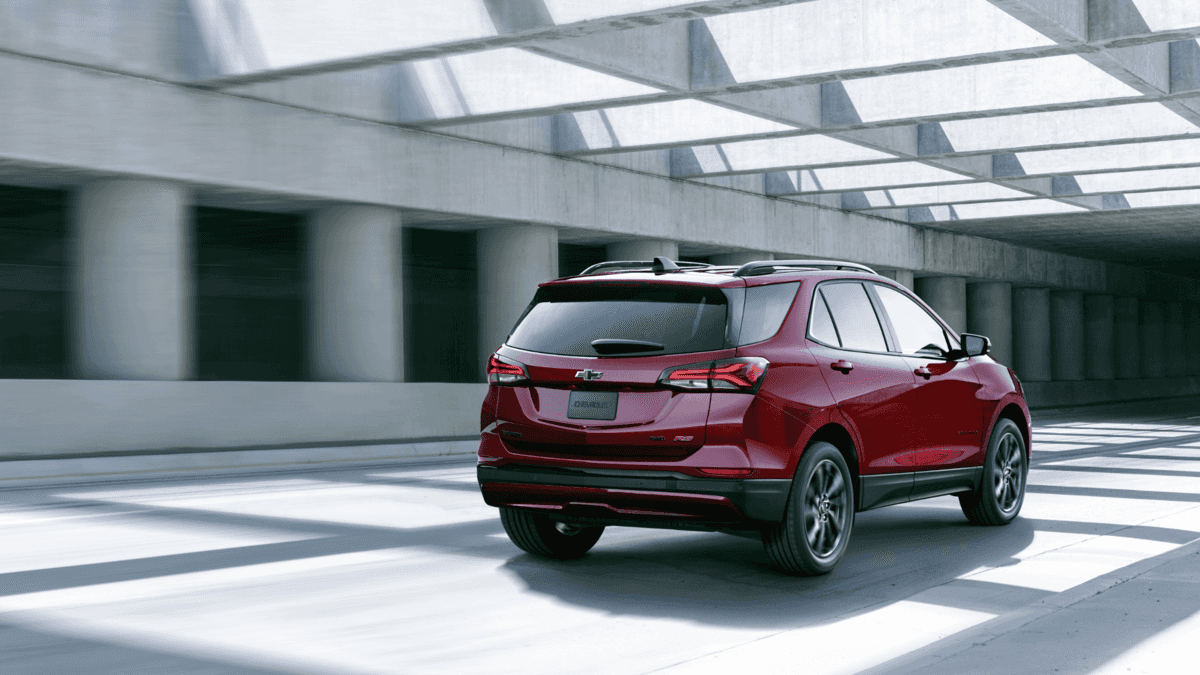 Rear view of a 2024 Chevrolet Equinox in red, driving through a modern, sunlit underpass. Perfect for exploring the various trims available in Forest City, NC.
