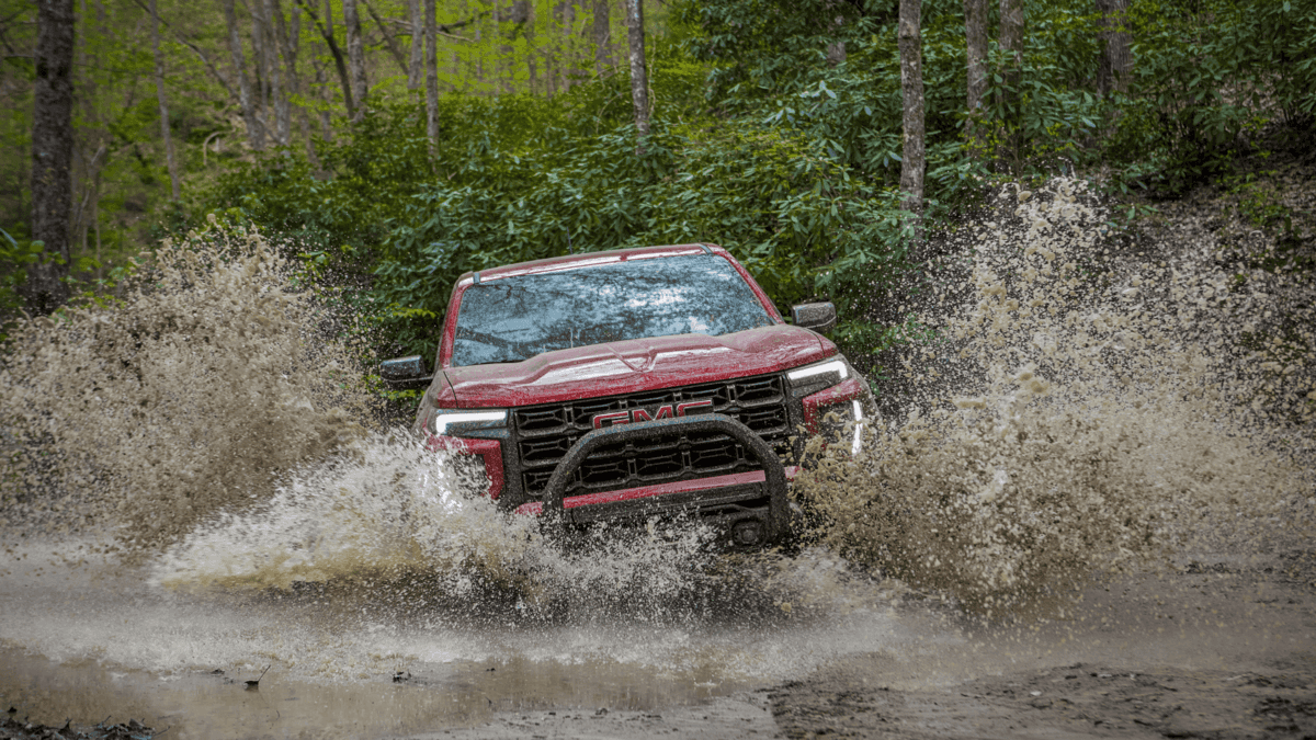 2024 GMC Canyon splashing through muddy terrain, showcasing its off-road capabilities. Highlighted in 'Top 5 Accessories for the 2024 GMC Canyon You Need in Forest City.