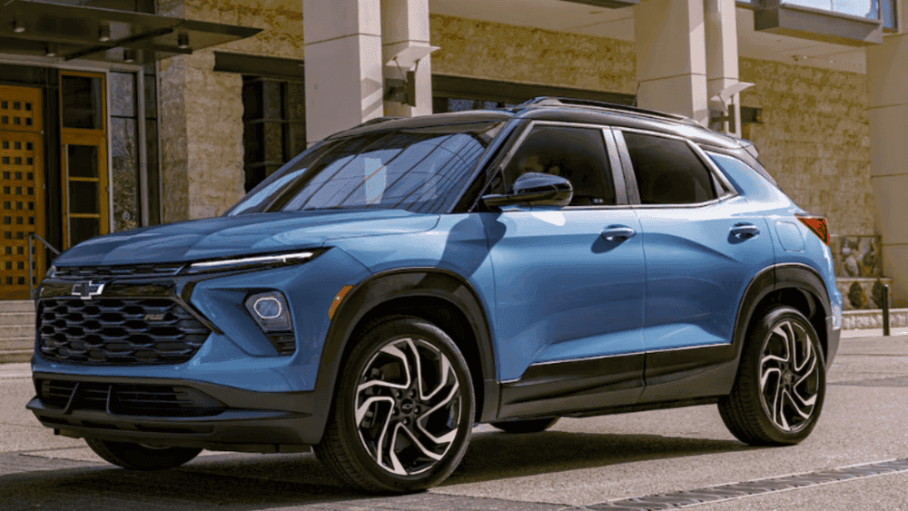 Exterior side view of a blue 2026 Chevrolet Trailblazer parked in an urban setting with sporty wheels and roof rails