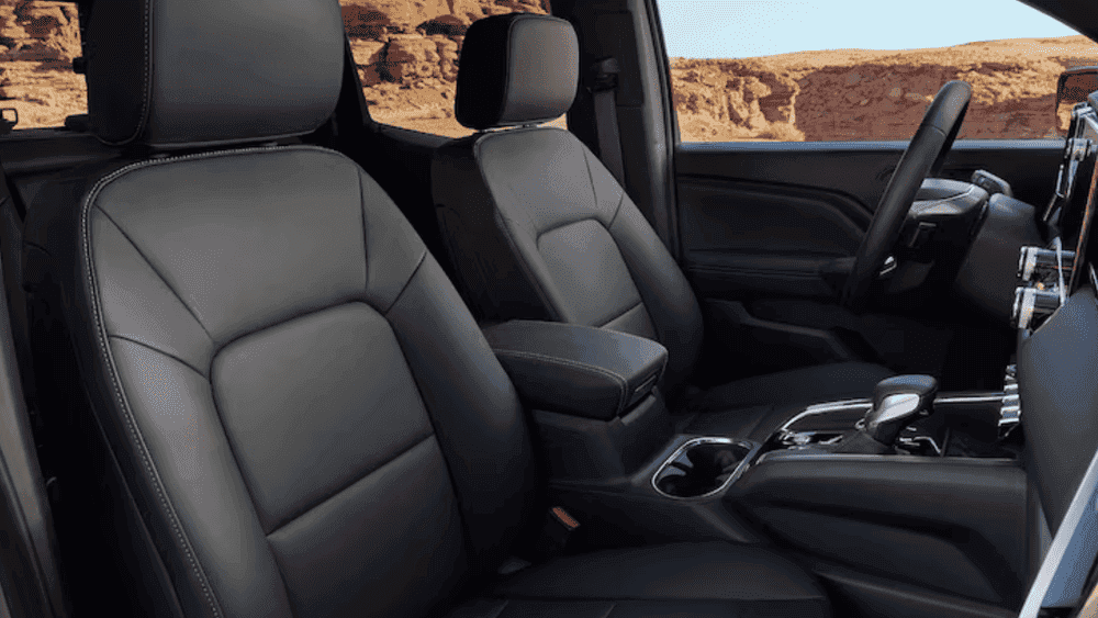 Interior seating view of a 2026 GMC Canyon showing leather-trimmed front seats and center console storage