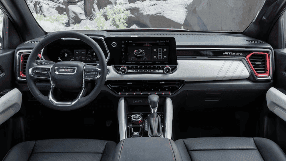 Front interior view of a 2026 GMC Canyon featuring a premium dashboard layout, touchscreen display, and rugged cabin design