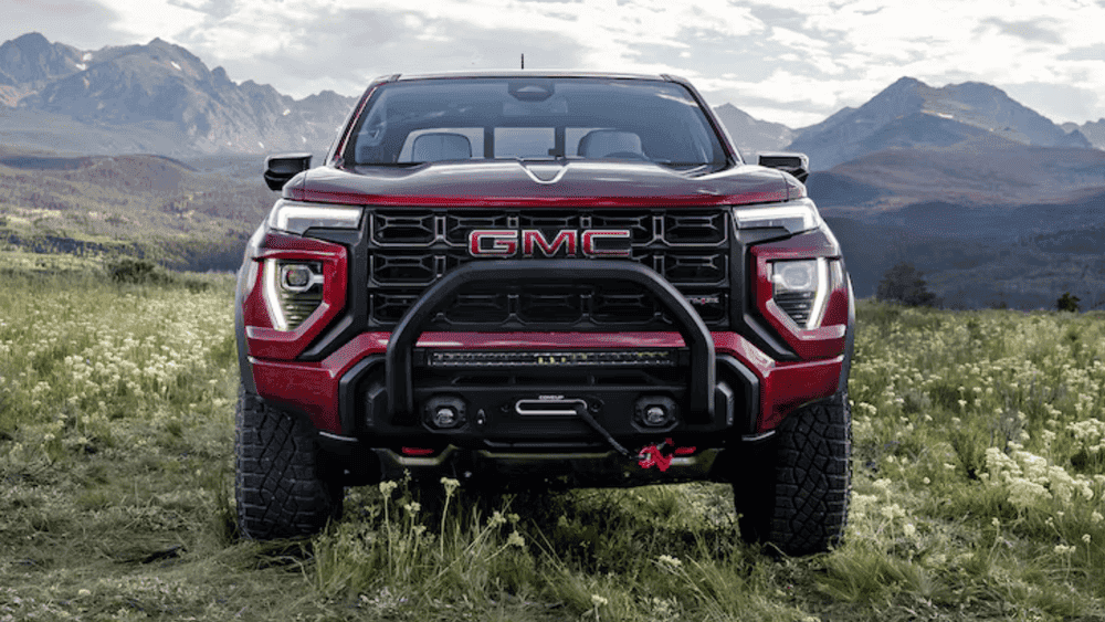 Front view of a red 2026 GMC Canyon with off-road bumper, aggressive grille, and trail-ready stance in a mountain setting