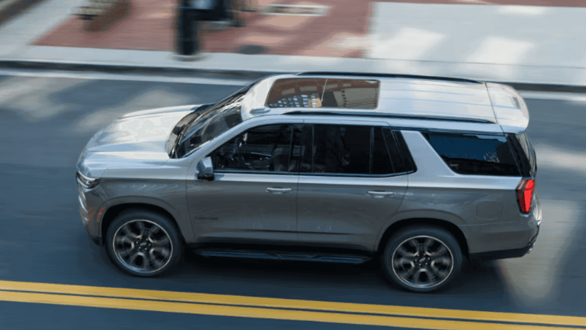 Exterior side view of a 2026 Chevrolet Tahoe driving through city streets, highlighting its full-size SUV profile and smooth ride