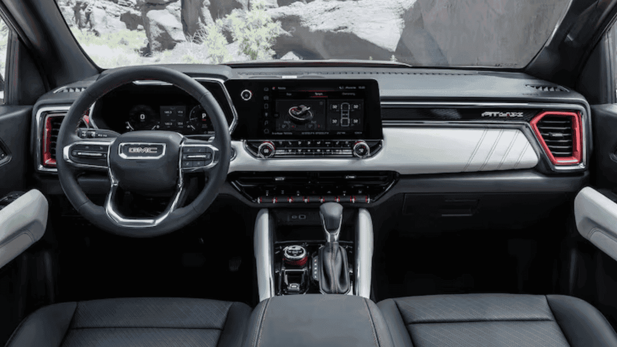 Front interior seating of a 2026 GMC Canyon with leather-trimmed seats, center console storage, and durable cabin materials