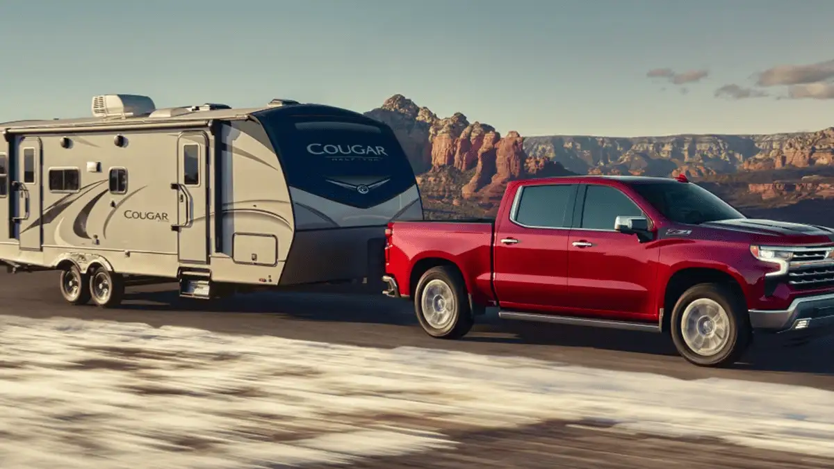 Red 2026 Chevrolet Silverado near Ruth, NC towing a travel trailer on an open highway, highlighting strong towing capability and road stability