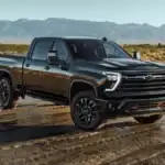 2026 Chevrolet Silverado HD near Ruth NC in gloss black finish with off-road tires parked on wet terrain with mountain backdrop