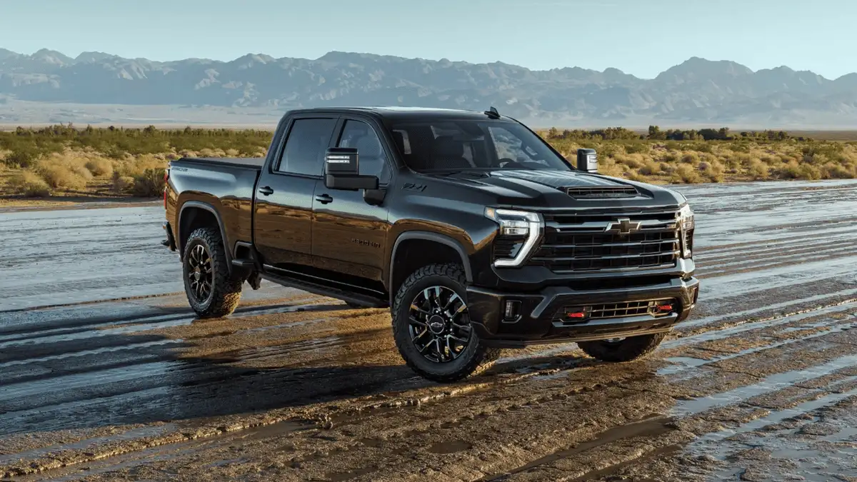 2026 Chevrolet Silverado HD near Ruth NC in gloss black finish with off-road tires parked on wet terrain with mountain backdrop