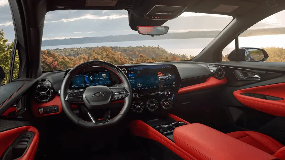2026 Chevrolet Blazer EV interior dashboard near Ruth NC featuring red and black two-tone cabin, dual digital displays, Bowtie steering wheel, and autumn lakeside view through windshield