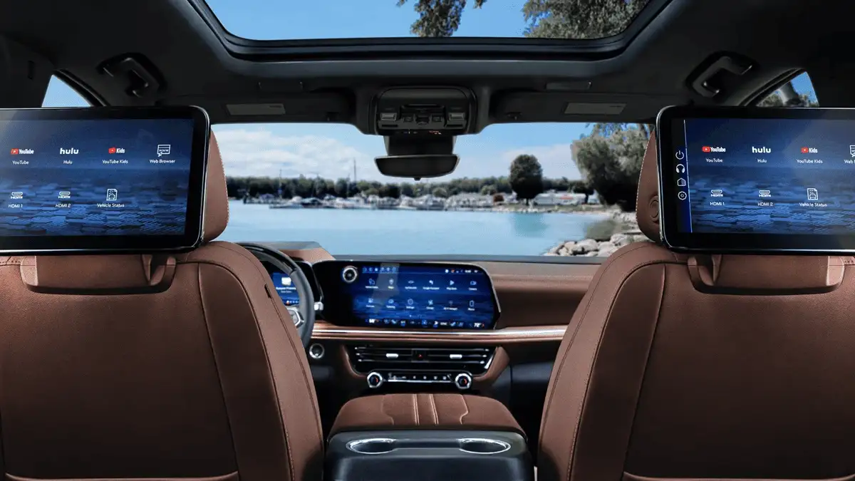 2026 Chevrolet Suburban rear cabin near Ruth NC featuring dual headrest-mounted entertainment screens showing YouTube and Hulu, brown leather seats, panoramic sunroof, and lakeside view