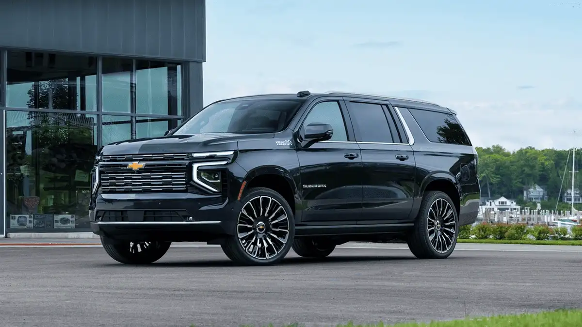 2026 Chevrolet Suburban High Country near Ruth NC in gloss black with chrome Bowtie grille, multi-spoke alloy wheels, and full-size SUV stance parked near a waterfront