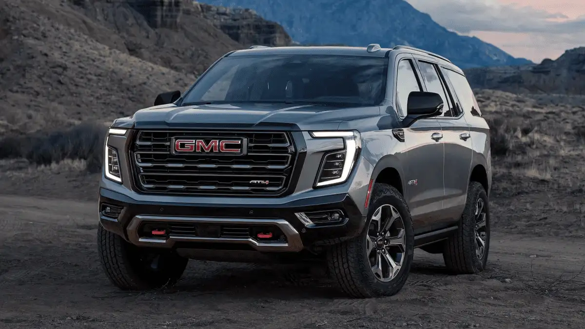 2026 GMC Yukon XL AT4 near Ruth NC in dark gray with bold red GMC grille lettering, AT4 off-road badging, LED headlights, and rugged terrain tires on rocky desert landscape