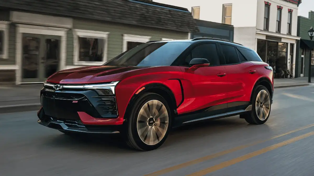 Plug in and head out with the 2026 Chevrolet Blazer EV around Ruth NC in red and black two-tone SS trim driving through a small town street with illuminated Bowtie grille and turbine-style alloy wheels