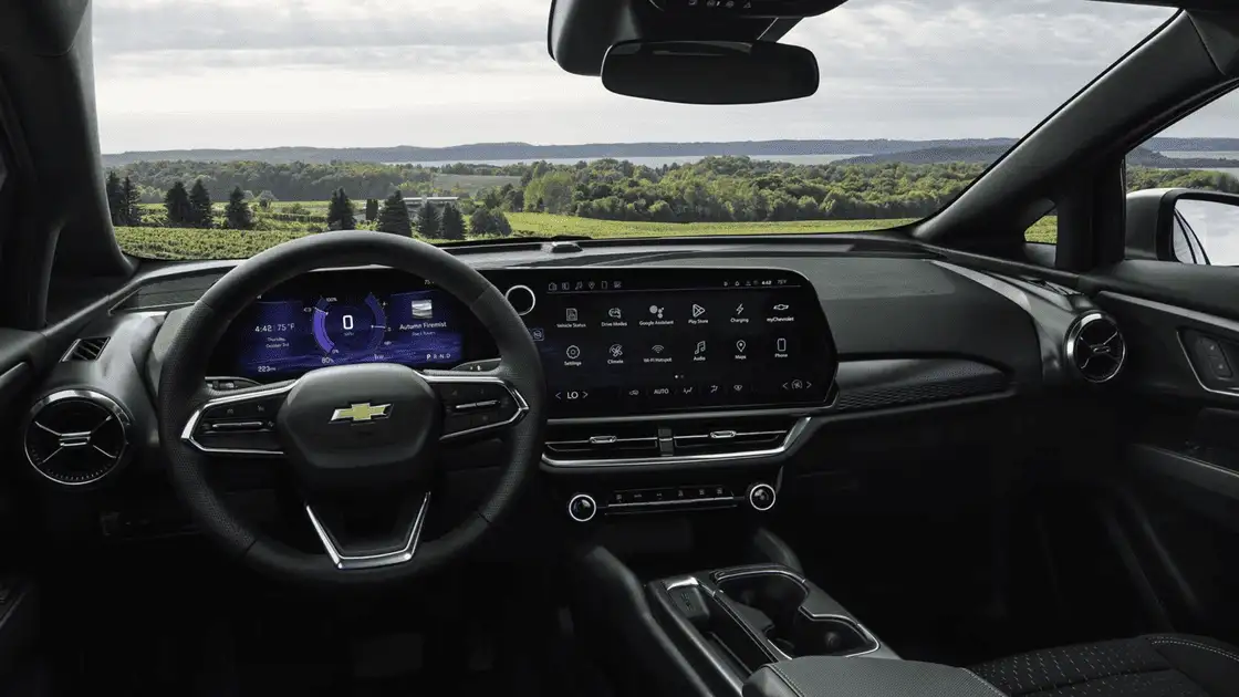 2026 Chevrolet Equinox EV interior dashboard near Ruth NC with Bowtie steering wheel, dual digital displays showing Google Assistant and charging status, and panoramic rural landscape through windshield