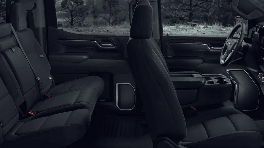 2026 GMC Sierra 1500 crew cab interior near Ruth NC showing spacious front and rear black cloth seating, center console with cup holders, and wooded landscape through windows