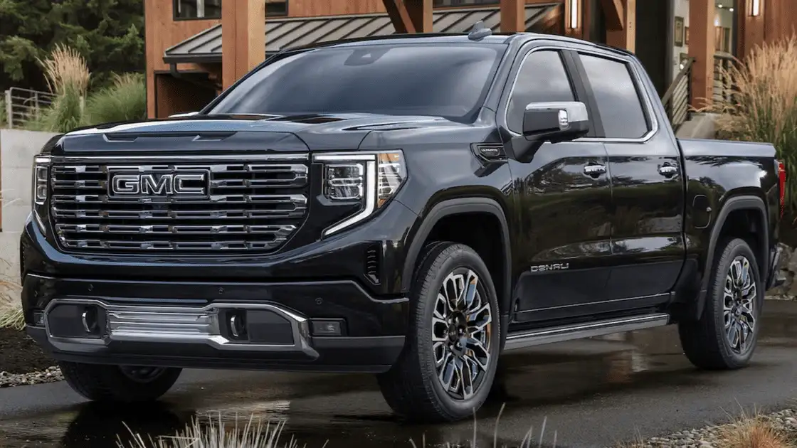 2026 GMC Sierra 1500 Denali near Ruth NC in gloss black with chrome GMC grille lettering, Denali badging, LED headlights, and multi-spoke alloy wheels parked outside a modern mountain lodge