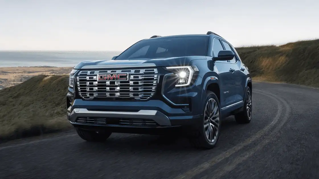 2026 GMC Terrain Denali near Ruth NC in dark steel blue with chrome GMC grille lettering, Denali badging, LED signature lighting, and premium alloy wheels on a coastal hillside road