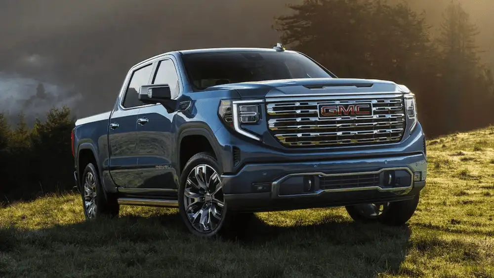 Smart storage and cabin features in the 2026 GMC Sierra 1500 near Ruth NC in steel blue Denali trim with chrome GMC grille lettering and polished alloy wheels parked on a grassy hillside at sunset