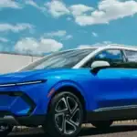 Why Ruth NC drivers are trading up to the 2026 Chevrolet Equinox EV in blue with white roof, illuminated Bowtie grille, Equinox badging, and multi-spoke alloy wheels parked near a green lawn