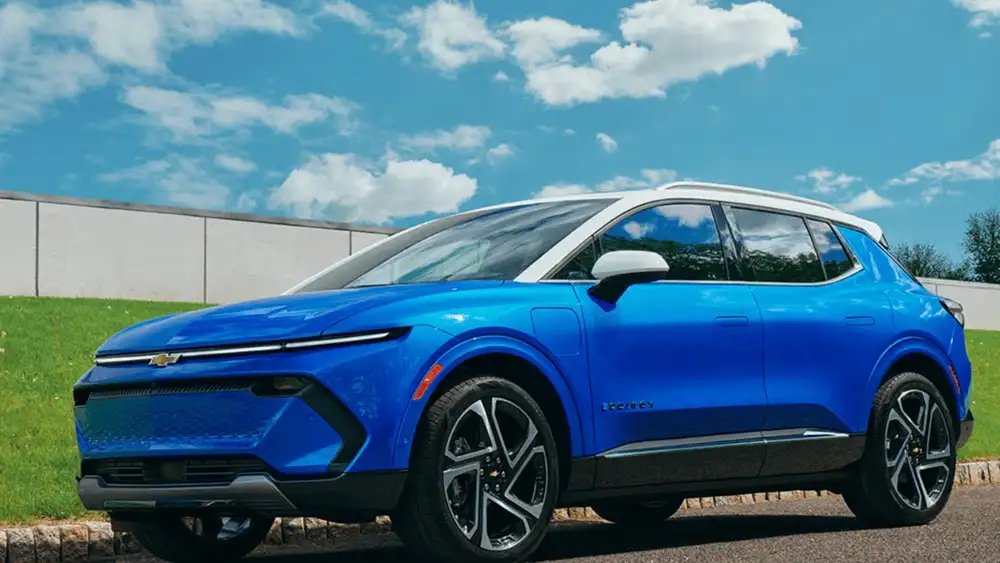 Why Ruth NC drivers are trading up to the 2026 Chevrolet Equinox EV in blue with white roof, illuminated Bowtie grille, Equinox badging, and multi-spoke alloy wheels parked near a green lawn