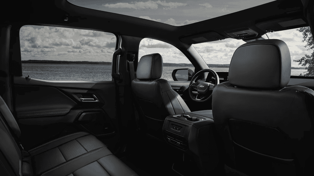 "2026 Chevrolet Silverado EV crew cab interior near Ruth NC showing spacious black leather front and rear seating with panoramic roof and lakeside view through windows "