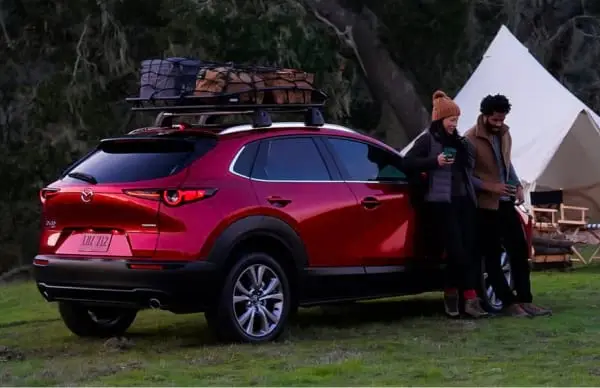 Couple are camping and are outside leaning against a brand new red Mazda SVU. 