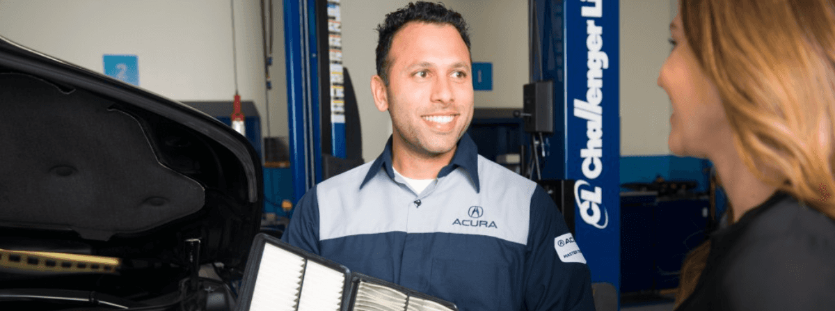 An Acura service technician showing a vehicle owner a dirty air filter and a new clean air filter