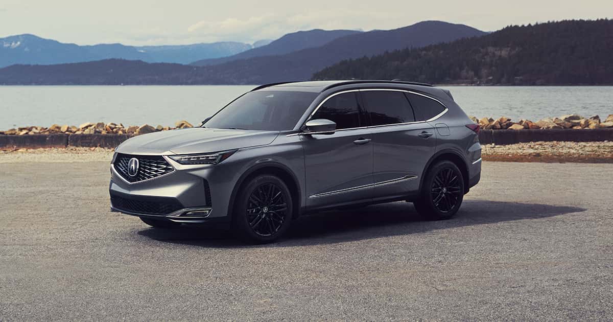 A silver Acura MDX with blacked-out wheels parked by a lake.