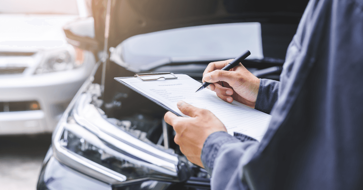 Mechanic writing on clipboard in front of car with open hood