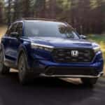 A Honda CR-V Hybrid in Canyon River Blue Metallic driving on a dirt road.