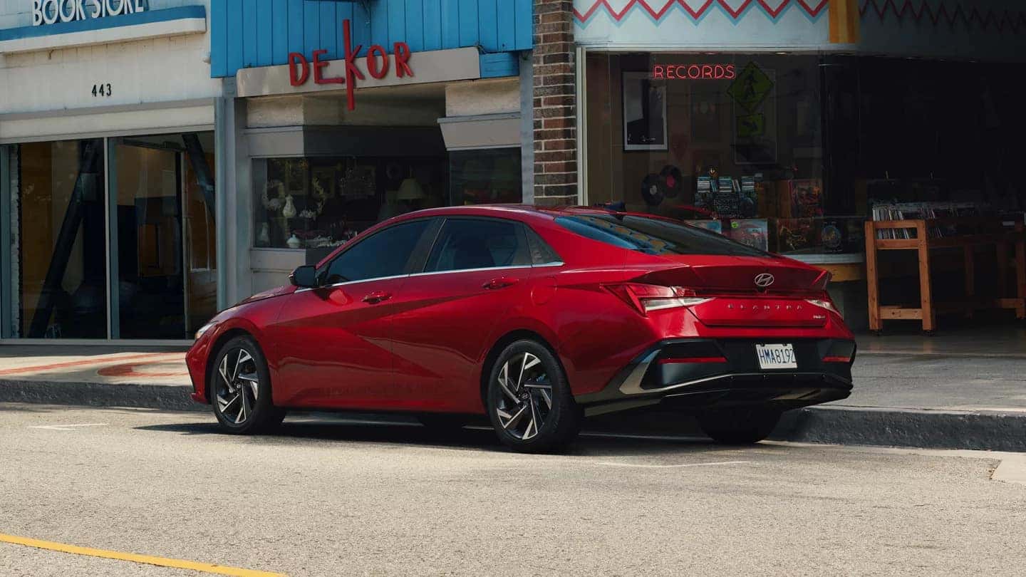A red Hyundai Elantra parked on the curb by a store front