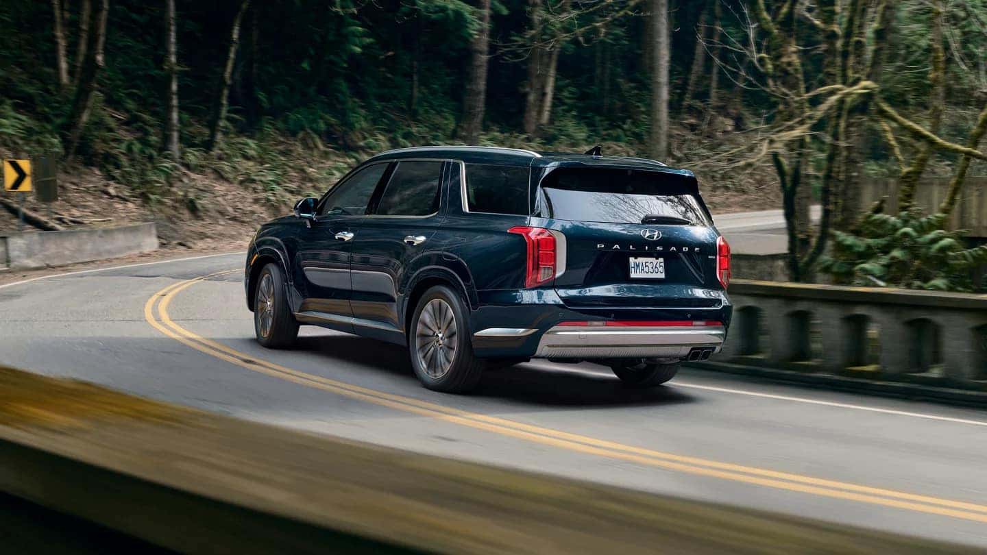 A blue Hyundai Palisade making a curve on the road in a forest