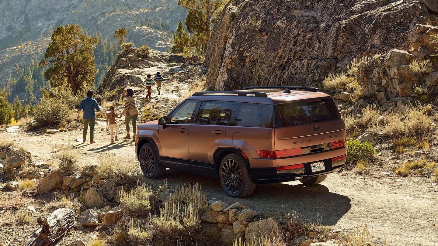 A brown Hyundai Santa Fe parked on a dirt road in a desert, with a family walking away from it down a trail