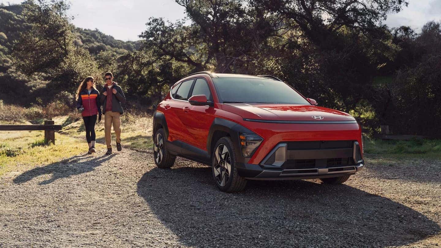 A red Hyundai Kona parked on dirt path with a couple approaching it