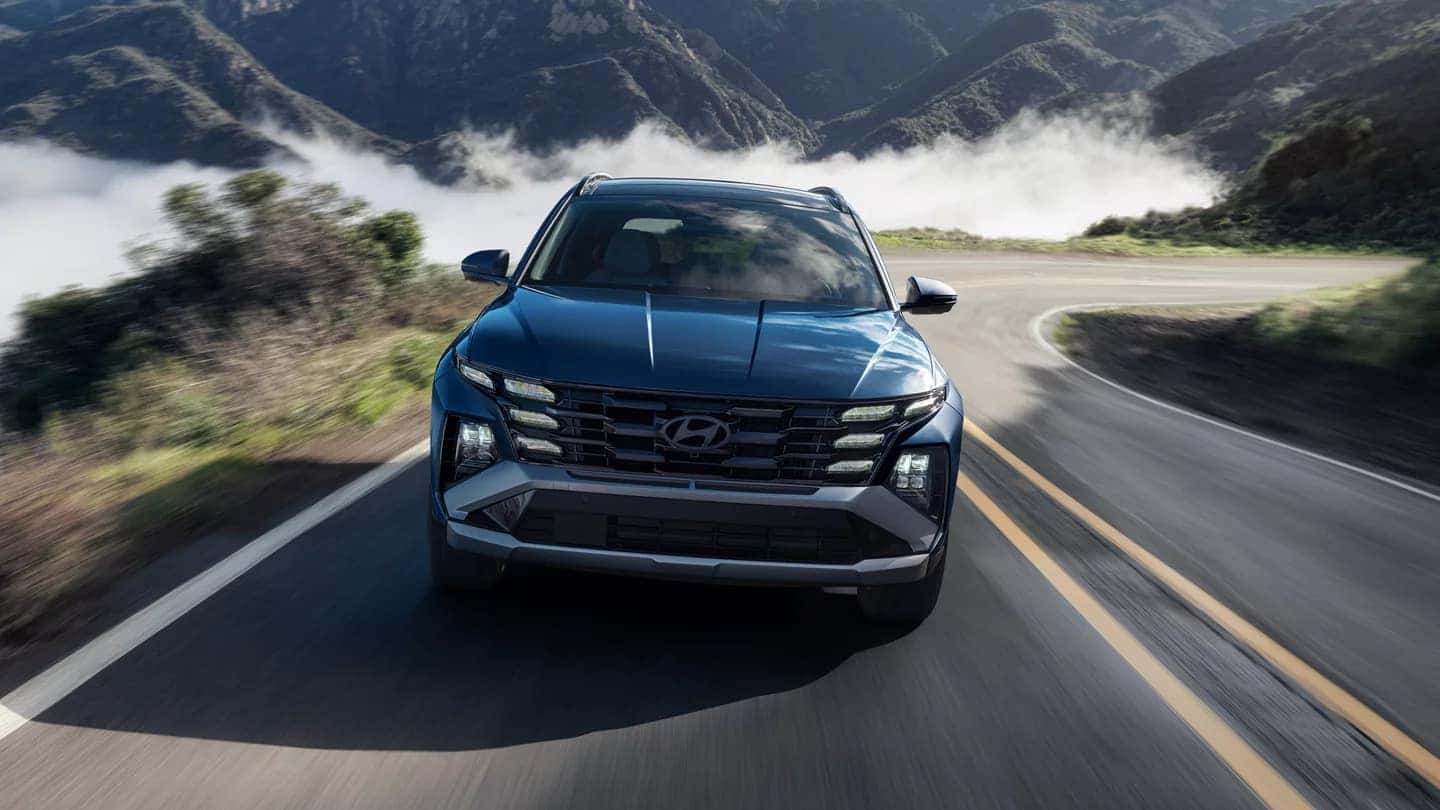 A front view of a blue Hyundai Tucson driving down the road in a mountain range