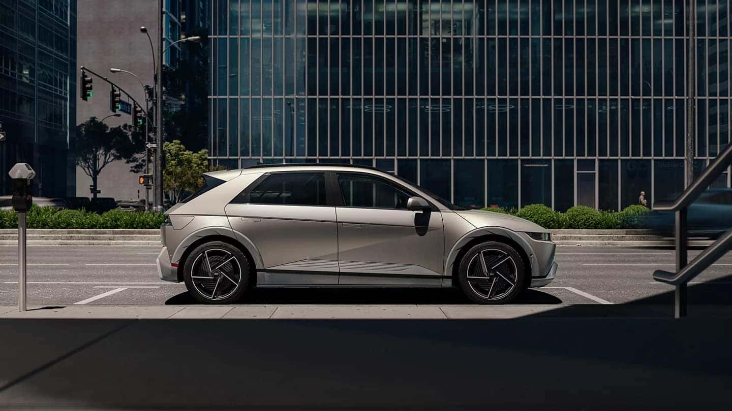 A light-colored Hyundai IONIQ 5 in profile, parallel parked in a city