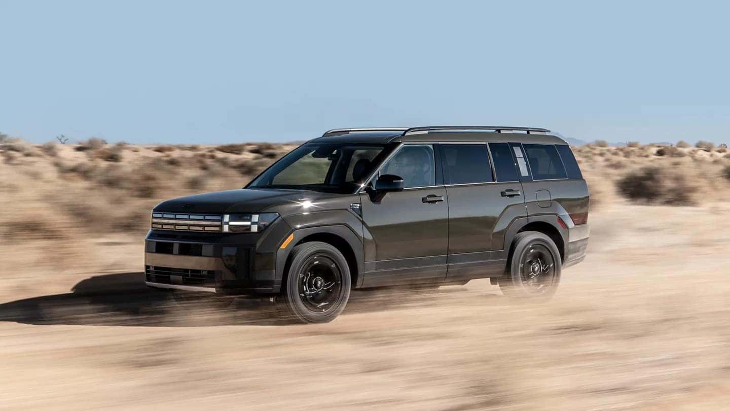 A dark grey Hyundai Santa Fe driving through a desert and kicking up dirt