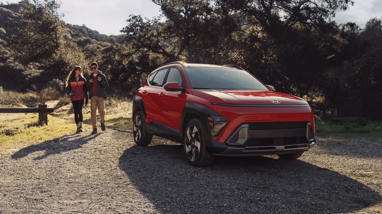 An orange Hyundai Kona Limited parked on gravel with two people behind it