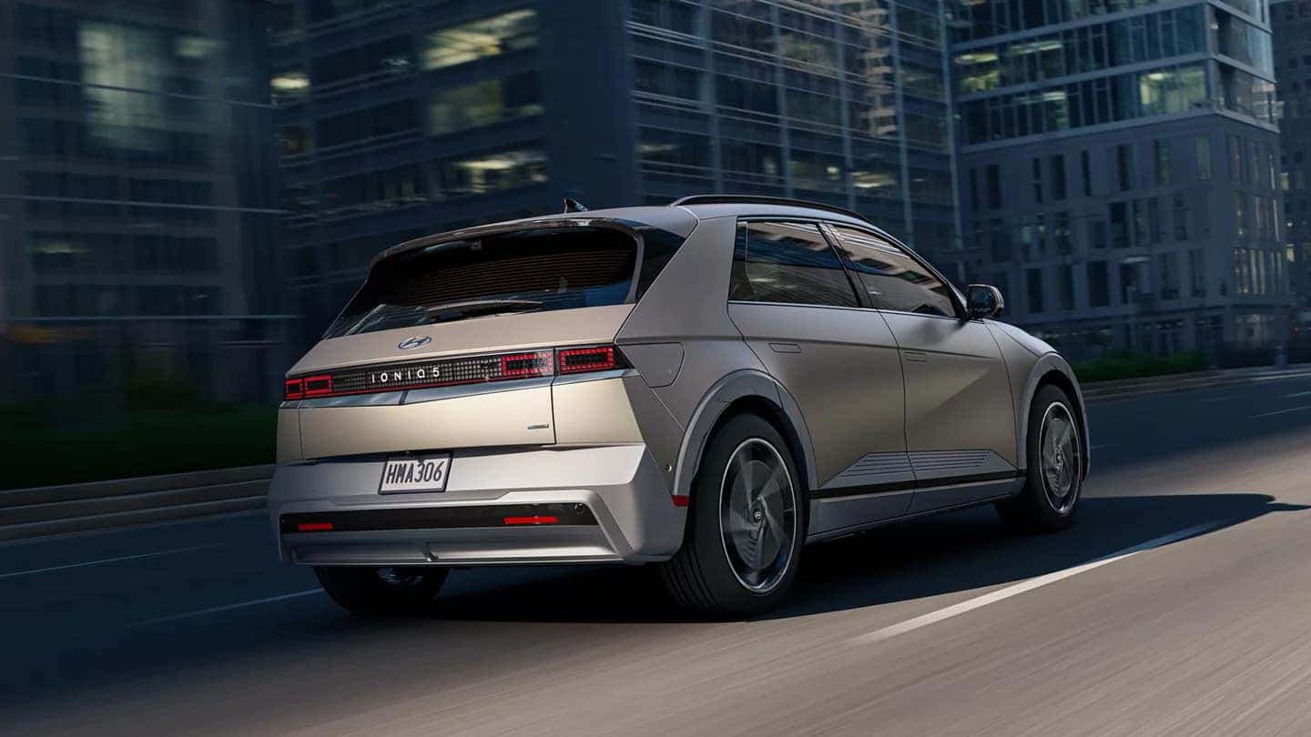 A sand-colored Hyundai IONIQ 5 driving down the road in a city