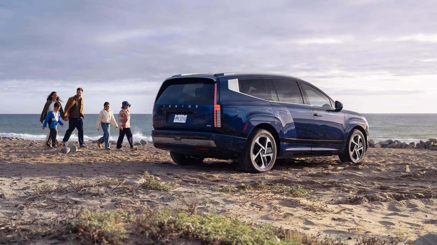 A blue Hyundai IONIQ 9 parked on a beach with a family approaching it