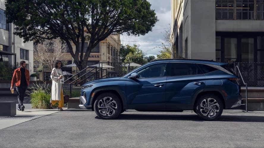 A blue Hyundai Tucson in profile parked by the curb in a city.