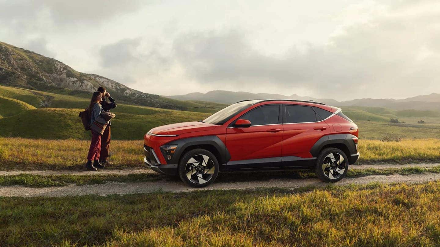 A red Hyundai Kona in profile on a dirt road with a couple walking up to it