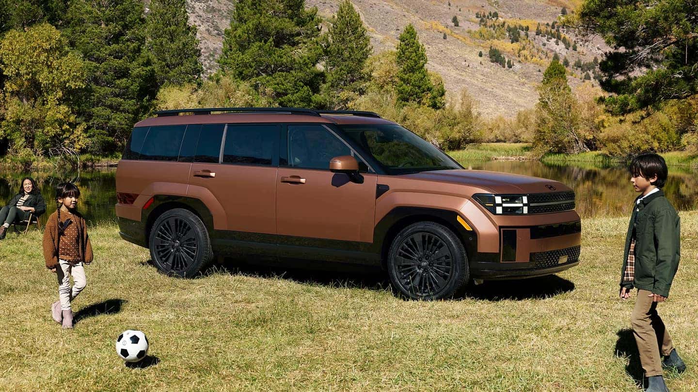 A brown Hyundai Santa Fe Hybrid in a field with a pair of children playing soccer near it